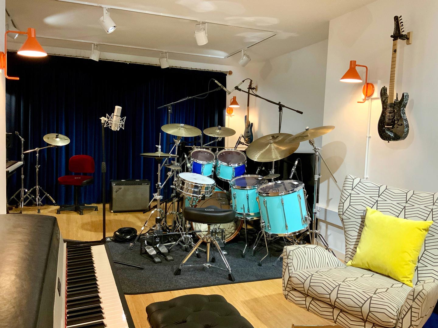 Recording studio with Rhodes piano, drum kit, grand piano, guitars, microphones, keyboard, spot lights.